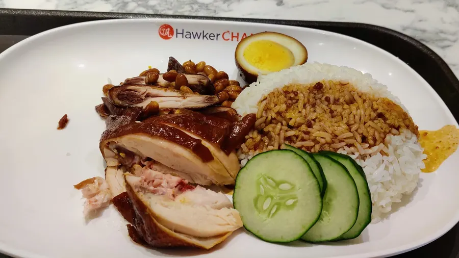 A plate of soy sauce chicken, rice, cucumber slices and a braised egg on a Hawker Chan tray