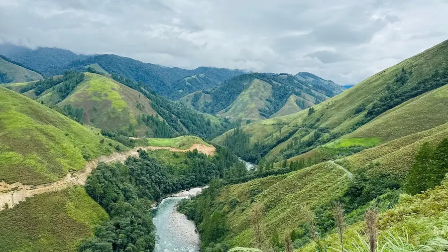 A river winding through steep green hills under a cloudy sky